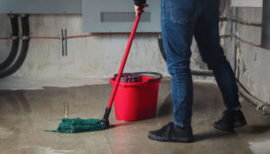 A person mopping up a leak on a concrete floor.